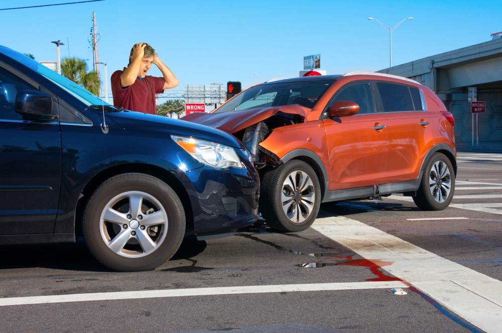 A man standing with his hands on his head next to two cars after an accident